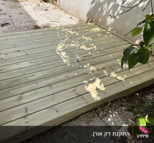 דק עץ מותקן בגינה עם צל עלים